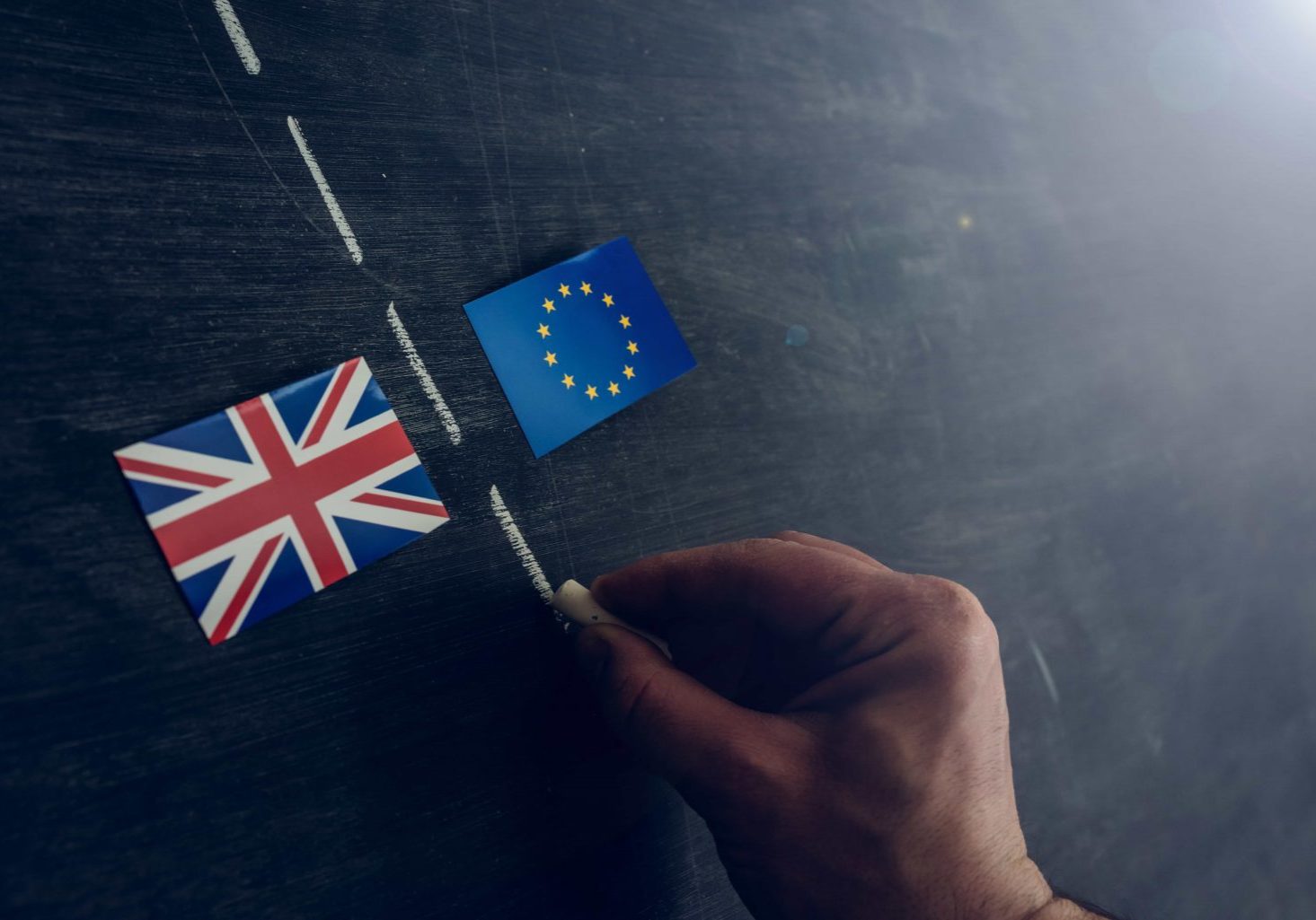 Hand drawing with chalk on blackboard a line to separate the Great Britain flag from the EU. Brexit concept